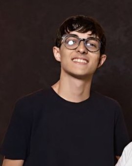 João Kairon, integrante da equipe Infotec, sorrindo, de óculos e camiseta preta.